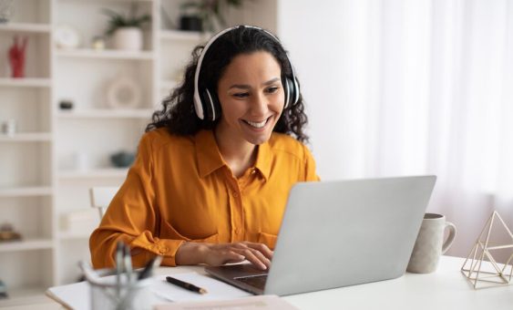 happy-brunette-businesswoman-using-laptop-wearing-earphones-working-workplace_116547-20880